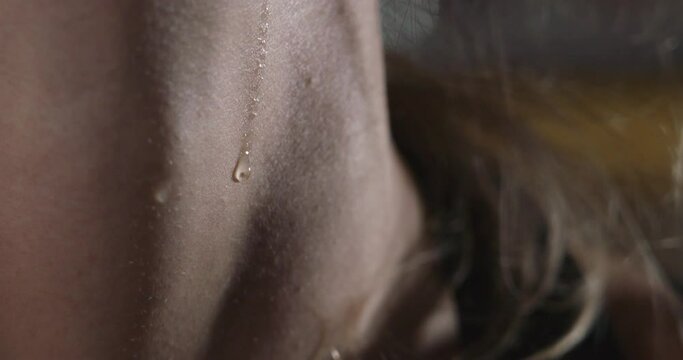 A macro shot is showing a drop of sweat gliding slowly down the throat of a blonde woman after she worked out.