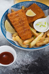 Closeup of deep-fried breaded fish fillet with french fries, vertical shot on a grey stone background