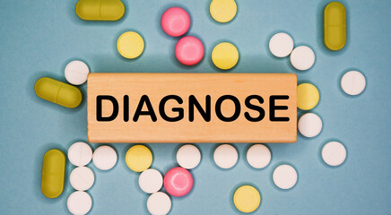 DIAGNOSE written on wooden block on a blue background among multicolored pills. Medical concept