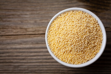 Yellow golden millet in white ceramic bowl on old wooden table with copy space.