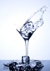 Water splashes. Fall of ice cubes in a wineglass with clear water on a white background