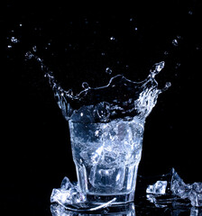 Splashes of water. Falling ice cubes into a glass of water on a black background