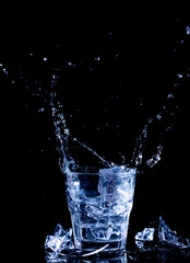 Water splashes. Fall of ice cubes in a glass with clear water on a black background