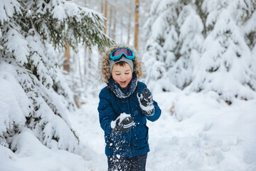 boy in a ski suit and ski goggles stands on a ski slope. Child in winter in the forest	