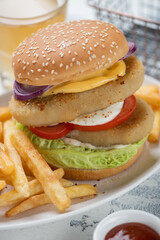 Closeup of double burger with sesame bun, fish cutlets, vegetables and french fries, vertical shot, selective focus