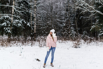 a beautiful girl in white fluffy mittens, a hat and light clothes with a surprised face and open mouth stands in a snowy park