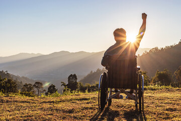 Happy disabled handicapped man is sitting on wheelchair at sunset.