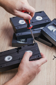 A man takes apart an old videotape and uses a screwdriver to unscrew the bolts from the case. Old technologies.