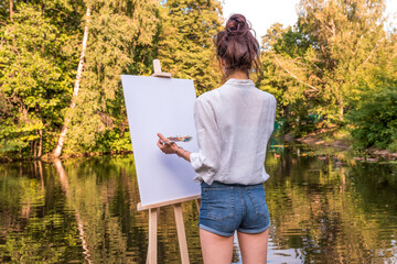 girl artist view from back, woman draws a picture, summer park lake pond river, creating creativity artistic mood. Blank white canvas, getting started. Water trees grass background.