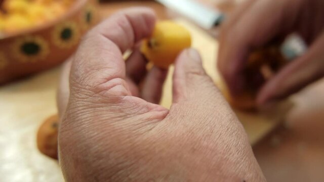 Hands carefully peeling Mexican hawthorns above cutting board