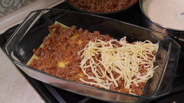 A woman in the kitchen prepares lasagna: pasta of lasagna, adds cheese, red minced meat sauce (bolognese) and white sauce (bechamel). Cooking lasagna