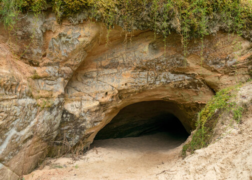 sandstone rock wall and entrance to the cave, the cave is located on the bank of a small river