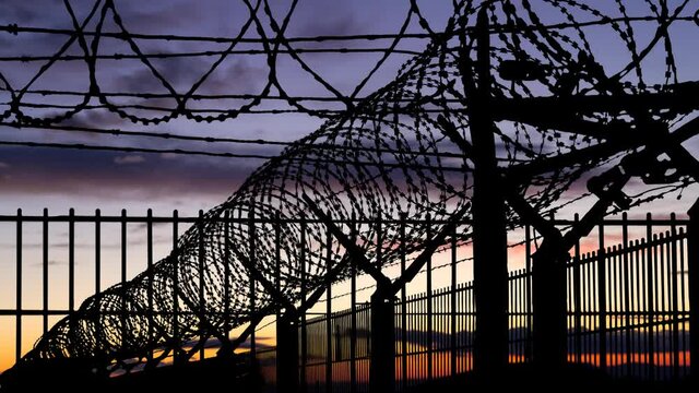 Conceptual Image with Wall of Mesh Steel and Barbed Wire, Time Lapse at Twilight, Concept of Confine, Prison