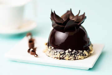 Chocolate sphere with almonds French pastry on white plate with chocolate curls, aside a white cup of coffee over a light blue background.