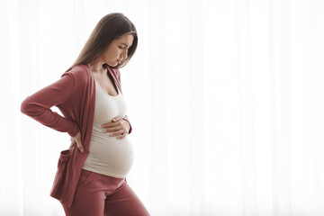 Pregnant woman with contractions, feeling unwell while standing near window at home