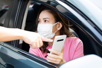 Woman wearing face mask sitting at driver seat of  a car and asking way with mobile phone