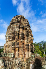 Fototapeta premium Face tower in the Bayon temple in Angkor over blue sky. Cambodia. Vertical view.