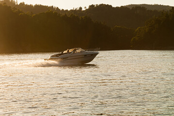 Naklejka premium A motorboat speeding over a fjord at sunset..