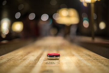 Red puck approaching the 3 point zone of a shuffleboard table..