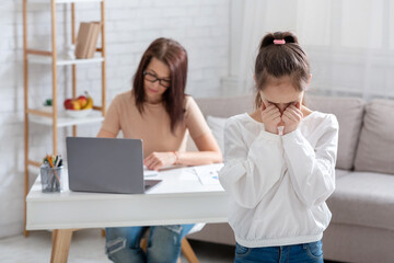 Upset teen girl crying, feeling lonely while her busy mother working online from home during covid-19 lockdown