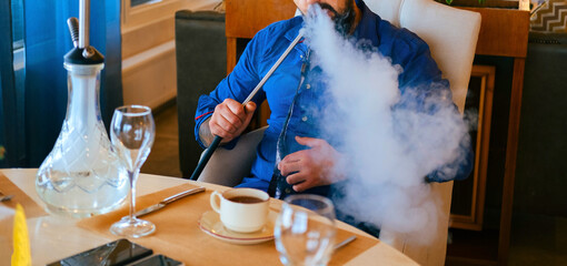 Selective focus unrecognizable bearded man smoking hookah in a coffee shop.