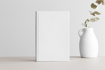 White book mockup with a eucalyptus in a vase on a beige table.