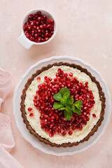 Homemade dessert chocolate tart with coconut cream and pomegranate and mint on a pink table background. Top view.