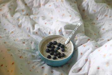 Bowl of porridge with cinnamon and blueberries, served on a bed. Selective focus.