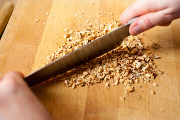Closeup of a chef chopping nuts with a knife on wooden table