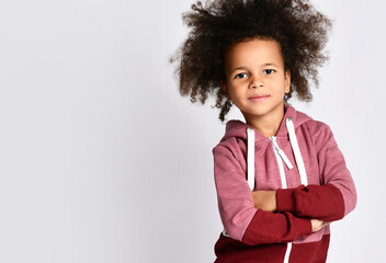 Studio shot of small cute African American black skin girl model with curly hair in sportswear, arms crossed over chest, posing for the camera, isolated on white background.