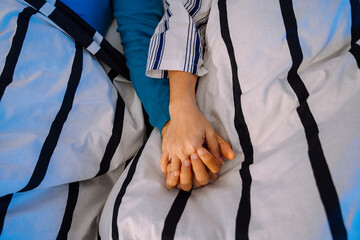 Senior couple holding hands on a bed.