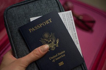 Travel kit with COVID-19 Vaccination Record card, Passport of USA on blurred red luggage...