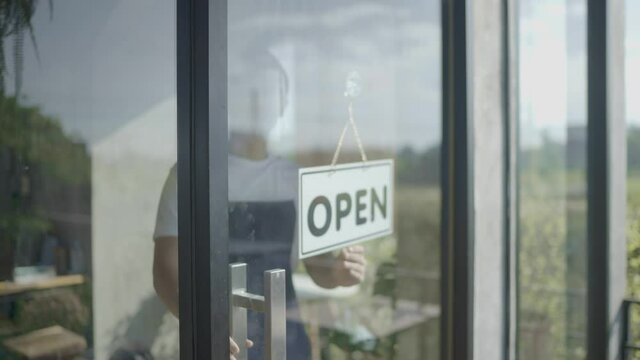 Cafe or restaurants and businesses reopen after the corona quarantine ends. An Asian man wearing a mask changed the sign from closed to opening the door. Small food store business following COVID blo