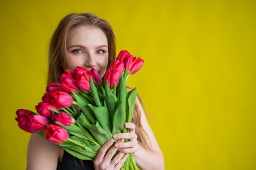 Fototapeta premium Woman with a bouquet of red tulips on a yellow background. Happy girl in a black dress holds an armful of flowers . Gift for Valentine's Day. The most romantic day of the year.