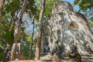 Fototapeta na wymiar Phayao, Thailand - Nov 29, 2020: Low Angle Buddha Statue Giving The First Sermon with 5 Disciples of The Buddha on Forest Backgroud in Wat Analayo Thai Temple