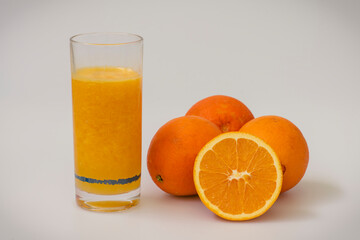 Vaso de jugo y naranjas, sobre fondo blanco.