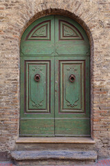 Close-up of the arched, green entrance door of an old brick house with stone steps, Tuscany, Italy