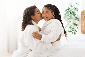 Loving Black Mom Kissing Her Daughter While Relaxing In Bathrobes At Home