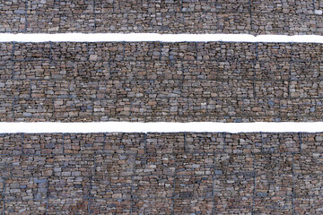 Metal Cage filled with rocks and snow texture . Stone wall with metal grid as background.  Gabion net
