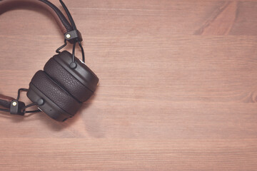 Wireless brown design headphones on wooden background laying in top corner. Side border from top view. Empty space for text. Copy space.