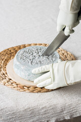 Male hands cutting whole round Head of blue cheese on light linen background. Farm homemade blue mold goat cheese.