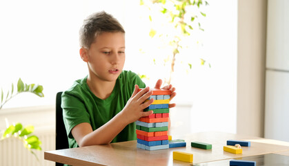 Focused boy in green t-shirt is playing  board game with colored blocks at home