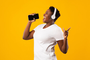 Plus-Size Black Woman In Headphones Singing Holding Smartphone, Yellow Background