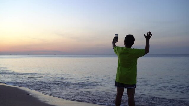 Happy time with Selfie on silhouette beach, Happy Asian Woman using Smartphone taking photos her cell phone at sea beach sunset for Relaxation in travel morning nature