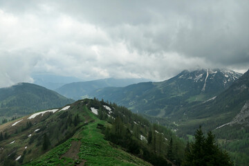 A panoramic view on the Alpine peaks in Austria from the Marstein. The slopes are still partially covered with snow. Stony and sharp mountains. Overcast. Baren slopes, green valley below. Serenity