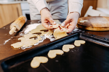 Cookies in shape of heart for the Saint Valentine's Day. Man is making heart shape cookies. Dough, flour and baking pan on the table.