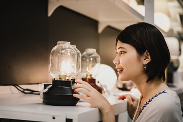 Asian young short hair beautiful woman choosing new lamp to buy at furnishings lighting store