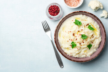 Mashed cauliflower with butter, pink peppercorns and parsley on concrete background