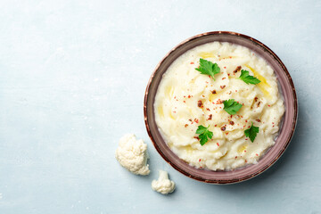 Mashed cauliflower with butter, pink peppercorns and parsley on concrete background