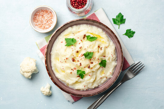 Mashed cauliflower with butter, pink peppercorns and parsley on concrete background